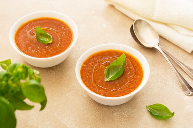 Gazpacho cold tomato soup bowls with basil and two spoons on light background