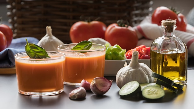 Gazpacho in due ciotole di vetro insieme ai suoi ingredienti