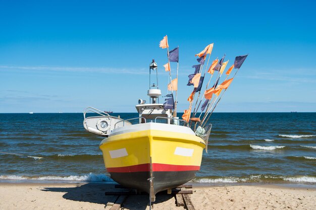 Foto danzica, polonia - 19 settembre 2016: barca o nave moderna imbarcazione marina con bandiere colorate sulla spiaggia in giornata di sole su sfondo blu mare e cielo