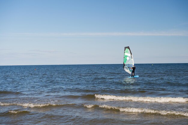 Gdansk, Poland - September 19, 2016: windsurfer or man sportsman surfs and sails on board by wind on sea water waves surface inshore on sunny day on blue sky