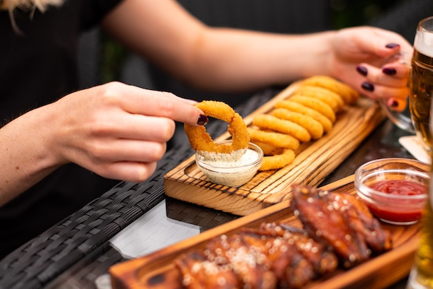 Geassorteerde biersnacks, fastfood. Bbq-vleugels en uienringen voorgerecht, gezouten kaas, vleeswaren, augurken, frites, nacho's, pistachenoten, chips en sausen met mok bier.