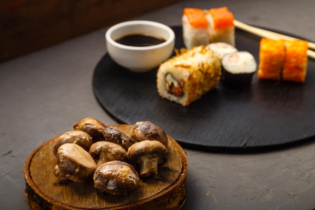 Geassorteerde broodjes op een rond bord naast stokken sojasaus en gebakken champignons op een zwarte