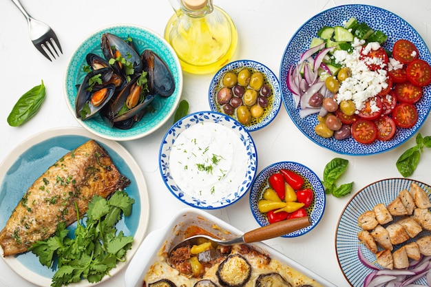 Geassorteerde Griekse gerechten op witte stenen achtergrond van bovenaf, moussaka, gegrilde vis, souvlaki, Griekse salade, gestoomde mosselen met kruiden, voorgerechten van Griekenland van bovenaf