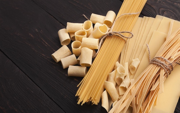 Geassorteerde handgemaakte pasta op zwarte houten achtergrond. Tagliatelle, spaghetti, cannelloni, garganelle en lasagne - verscheidenheid aan rauwe Italiaanse macaroni, kopieer ruimte