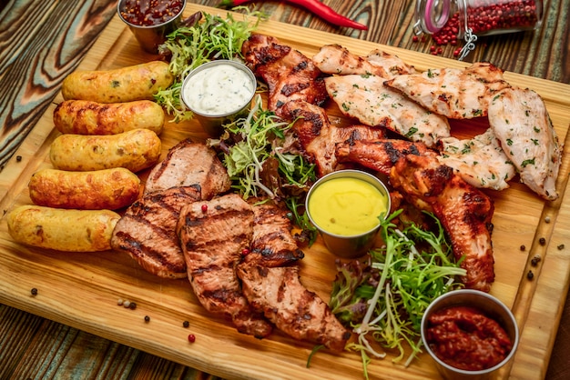 Geassorteerde heerlijke gegrilde vlees en groenten met verse salade en bbq saus op snijplank op hout