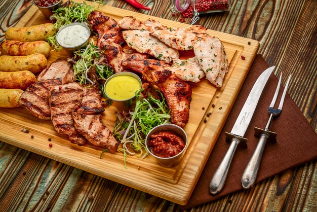 Geassorteerde heerlijke geroosterde vlees en groenten met verse salade en bbq saus op scherpe raad op houten achtergrond. Grote set warme vleesgerechten