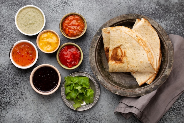 Geassorteerde Indiase chutneys in rustieke kommen en flatbread op grijze betonnen ondergrond. Bovenaanzicht van flatbread met kleurrijke chutney, traditionele Indiase sauzen en dipsauzen als snack of bijgerecht, close-up