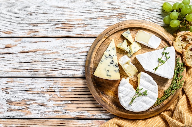 Geassorteerde kazen op een ronde houten snijplank. Camembert, brie en blauwe kaas met druiven.