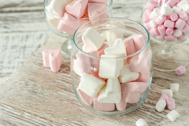 Geassorteerde roze en witte marshmallows in glazen bekers op houten achtergrond. Hartvormige marshmallow voor warme chocolademelk of cacao.