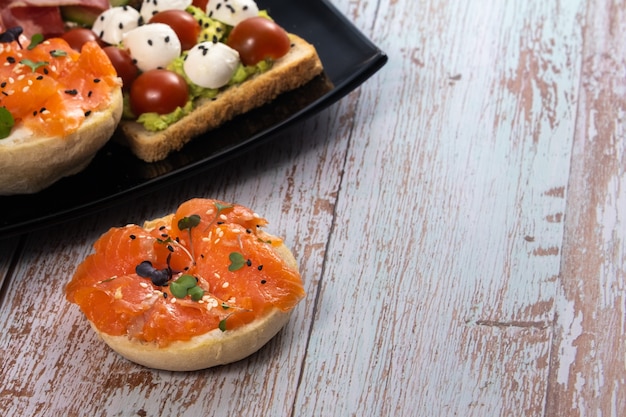 Geassorteerde sandwiches met vis, kaas, vlees en groenten op een zwarte plaat.