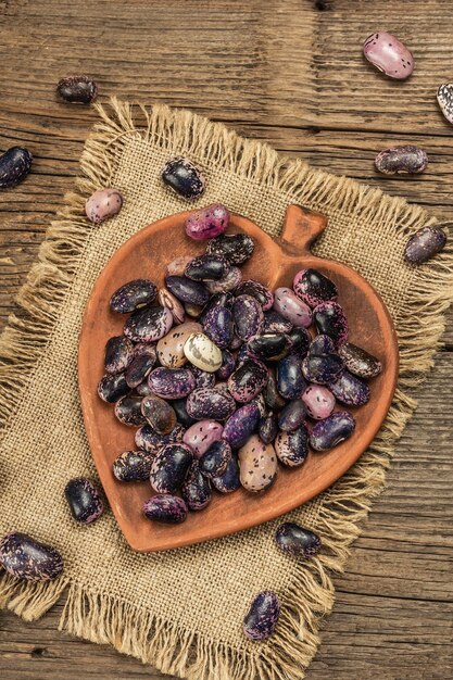 Geassorteerde veelkleurige bonen in een keramische kom. Ruw gezond ingrediënt voor het koken van nuttig voedsel. Oude houten tafel, bovenaanzicht