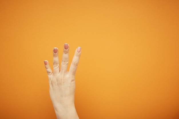 Gebaar, vrouwelijke hand toont vier vingers geïsoleerd op oranje.