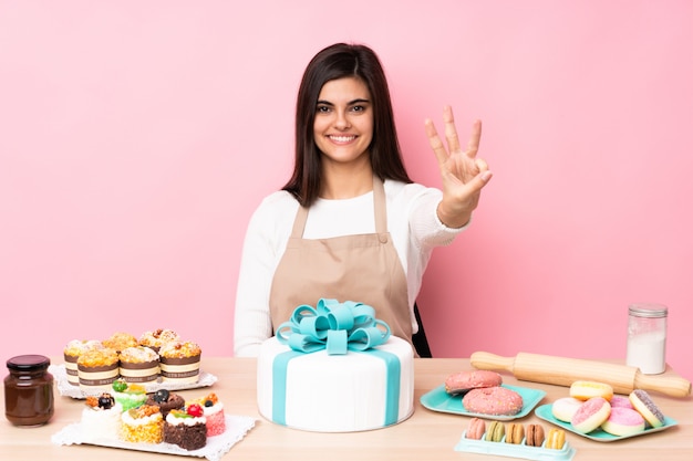 Gebakchef-kok met een grote cake in een gelukkige lijst en het tellen van drie met vingers