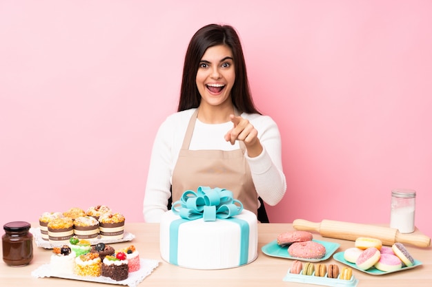 Gebakchef-kok met een grote cake in een lijst over roze verrast muur die en voorzijde richten