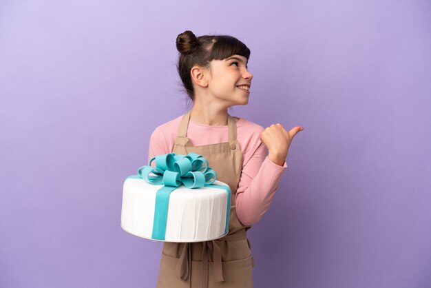 Gebakje meisje met een grote cake geïsoleerd op paarse achtergrond wijzend naar de zijkant om een product te presenteren