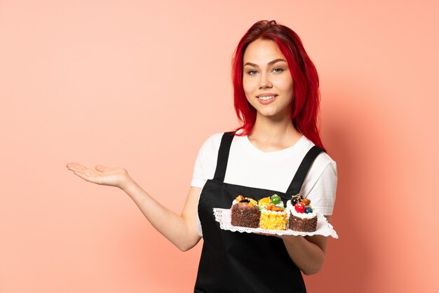 Gebakjechef-kok die muffins op roze muur houden die een idee voorstellen terwijl het kijken naar glimlachen