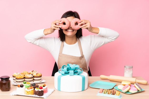 Gebakjechef-kok met een grote cake in een lijst over geïsoleerde roze muur