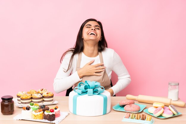 Gebakjechef-kok met een grote cake in een lijst over roze muur die veel glimlachen