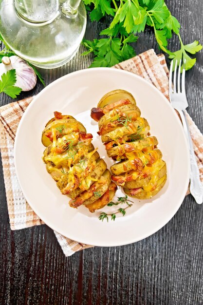 Gebakken aardappelen gelaagd met gerookt spek en kaas in een bord op een servet op een donkere houten plank van bovenaf