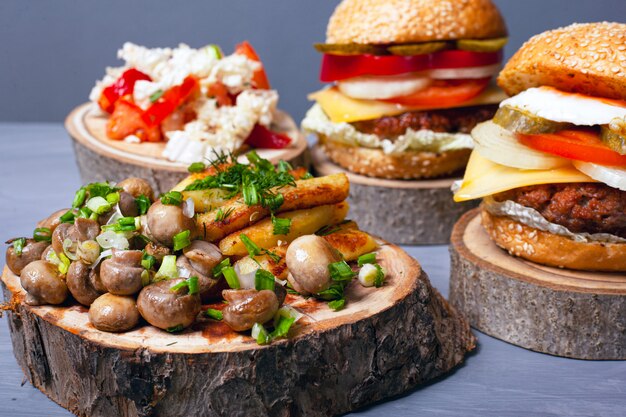 Gebakken aardappelen met champignons en sappige vleesburgers op houten stompen op grijze achtergrond. bos fast food.