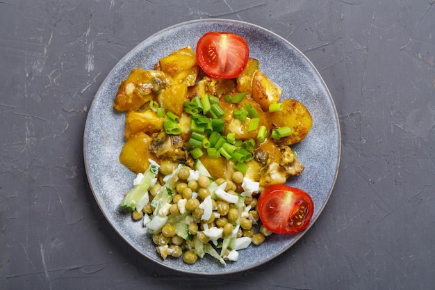 Foto gebakken aardappelen met kaas en champignons gegarneerd met kerstomaatjes bestrooid met groene uien in een bord op een grijze achtergrond