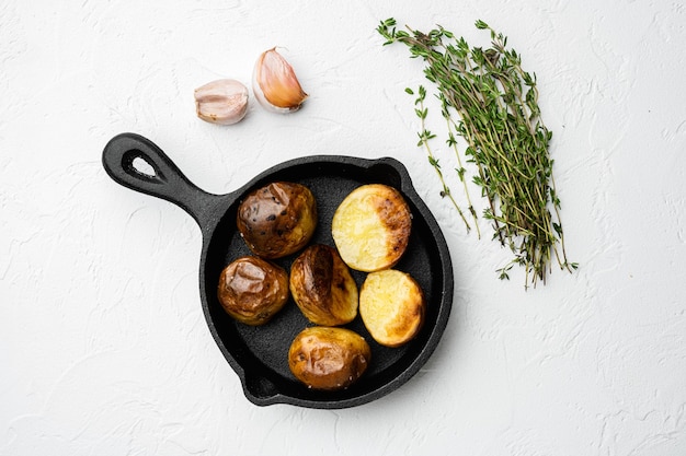 Gebakken aardappelen set, in gietijzeren pan, op witte stenen tafel achtergrond, bovenaanzicht plat lag