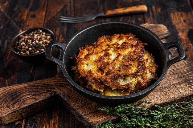 Gebakken Aardappelpannenkoekjes of Fritters met kruiden in een pan. Donkere houten achtergrond. Bovenaanzicht.