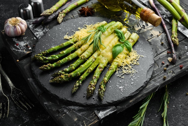 Gebakken asperges met kaas en basilicum op een zwarte stenen plaat Bovenaanzicht Vrije ruimte voor uw tekst