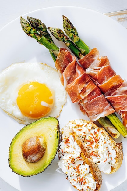 Gebakken asperges verpakt in jamon gebakken eieren bruschetta met zachte kaas en avocado op een wit bord