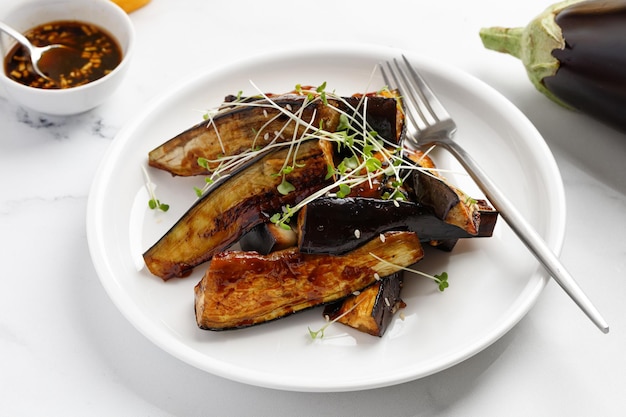 Gebakken auberginesticks in het glazuur met sojasaus en honing gegarneerd op wit bord