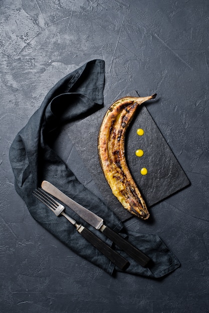 Gebakken bananen met honing op een zwarte stenen bord.