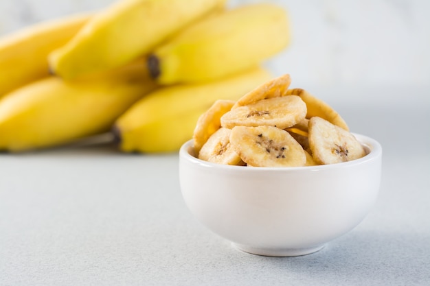 Gebakken bananenchips in een witte kom en een tros bananen op tafel. fast food. detailopname