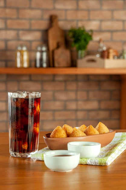 Gebakken Braziliaanse kroketten coxinha de frango met ijskoude frisdrank in een keuken met bakstenen muur