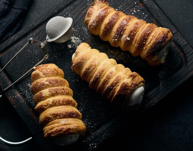 Gebakken buisjes gevuld met opgeklopte eiwitroom op een zwarte houten keukenplank