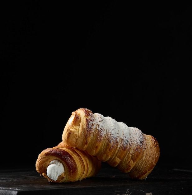 Gebakken buisjes gevuld met opgeklopte eiwitroom op een zwarte houten keukenplank