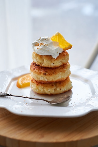 Gebakken cottage cheese tortilla's, sirniki met zure room en sinaasappelschil geserveerd op een witte plaat