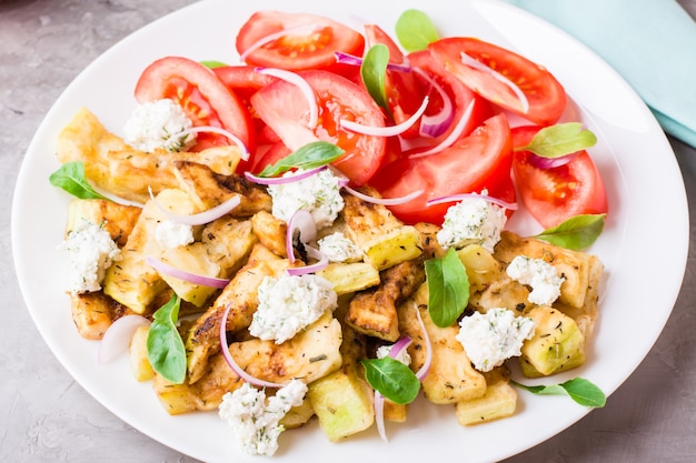 Gebakken courgette met feta-kaas, tomaten, kruiden en uien op een bord