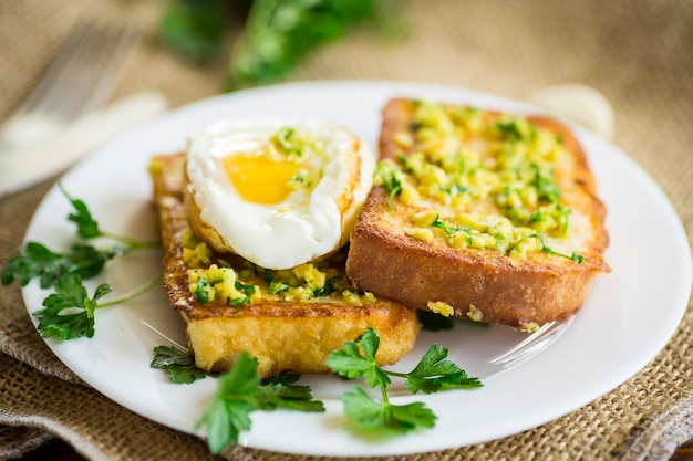 Gebakken croutons in beslag met knoflook en kruiden en een gebakken ei in een bord op een houten tafel