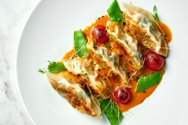 Gebakken dumplings of Japanse Gyoza in gele saus, kerstomaatjes en groene erwten, geserveerd in een witte plaat op een marmeren tafel. Pan-Aziatische keuken. Restaurant eten