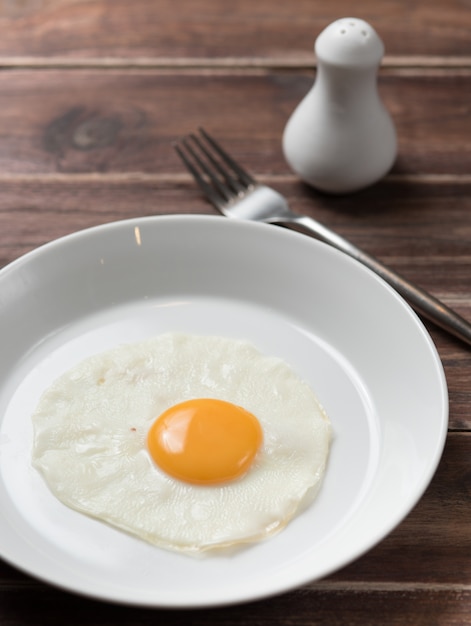 Gebakken ei in witte plaat met vork op houten tafel