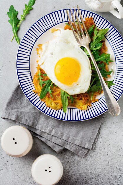 Gebakken ei met aardappelpannenkoek, rucola en avocado op keramische plaat voor ontbijt. bovenaanzicht.