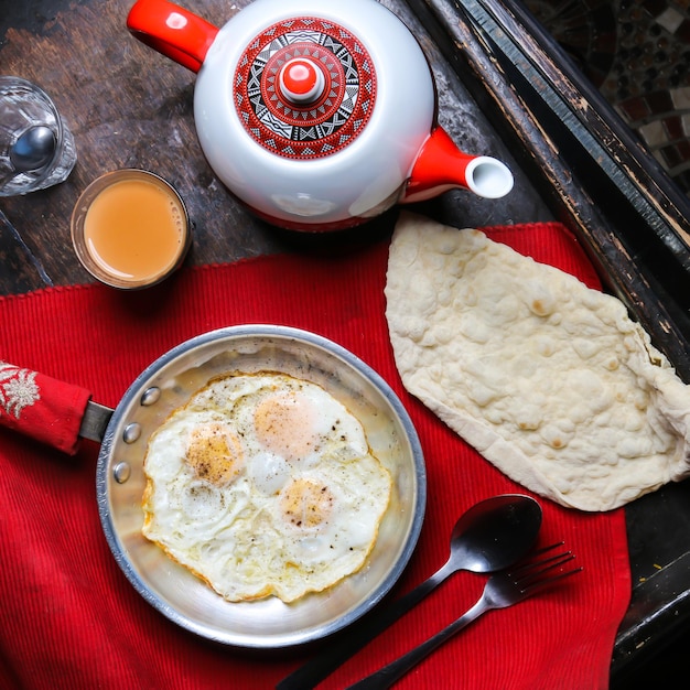 Gebakken ei met brood, koffie en theepot geserveerd in schotel geïsoleerd op rode mat bovenaanzicht op tafel Arabisch eten
