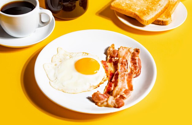 Gebakken ei met geroosterd spek zwarte koffie toast op gele achtergrond Retro Amerikaans ontbijt Harde schaduw