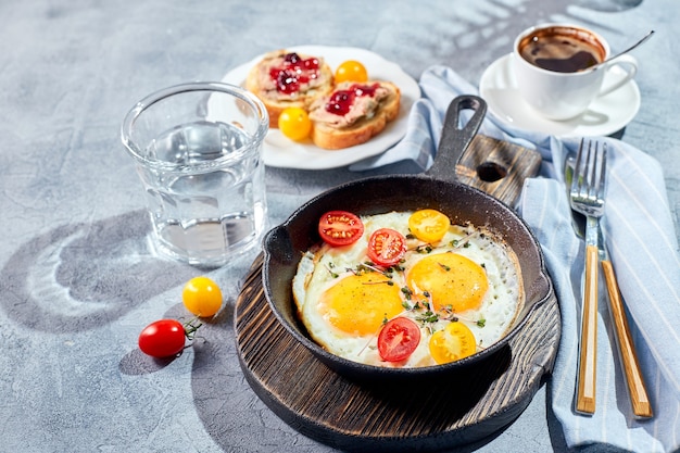 Gebakken eieren. Gebakken eieren van twee eieren in gietijzeren pan met kerstomaatjes en microgreens, toast en kopje koffie. Zonnig ochtendontbijtconcept