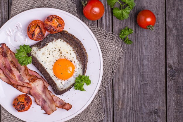 Gebakken eieren in roggebrood met spek, tomaten en peterselie in rustieke stijl.