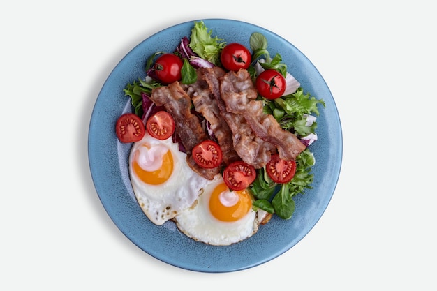 Gebakken eieren met bacon, sla en cherrytomaatjes op een blauw bord geïsoleerd op een witte achtergrond Bovenaanzicht Flat lay