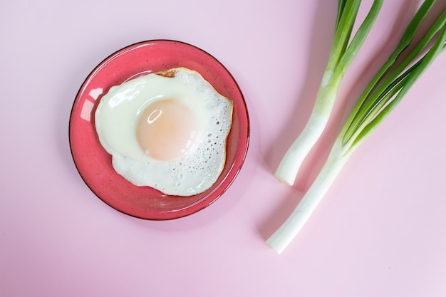 Gebakken eieren met groene uien op een roze achtergrond