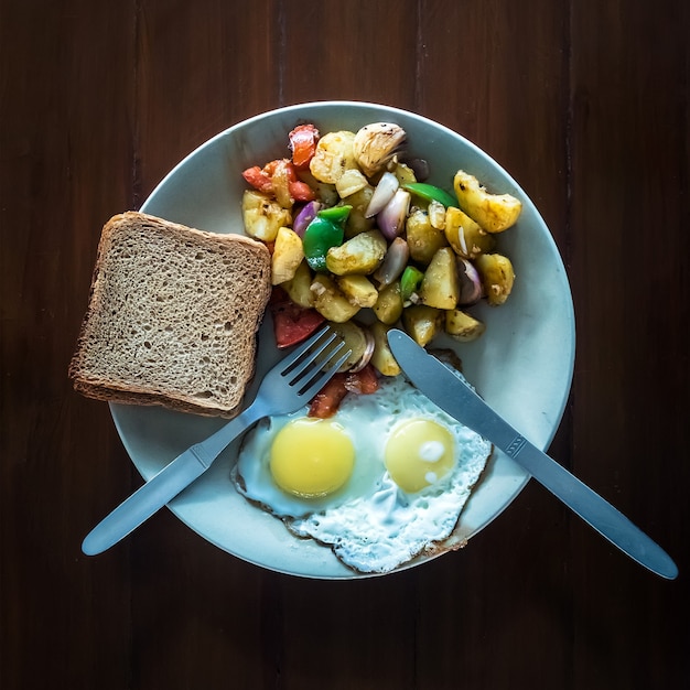 Gebakken eieren met groentestoofpot en knapperige toast in een bord. het uitzicht vanaf de top. een vegetarisch ontbijt. het proces van eten.
