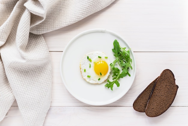 Gebakken eieren met rucola in een bord brood en linnen handdoek op een houten tafel