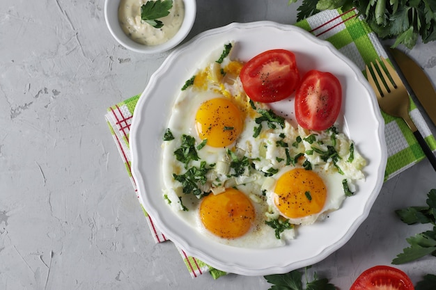 gebakken eieren met selderij en peterselie op een witte plaat, geserveerd met tomaten. gezond ontbijt